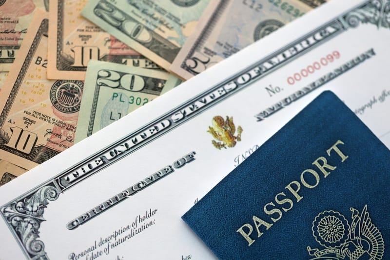 A U.S. Certificate of Naturalization and a blue U.S. passport on top of a pile of American currency.