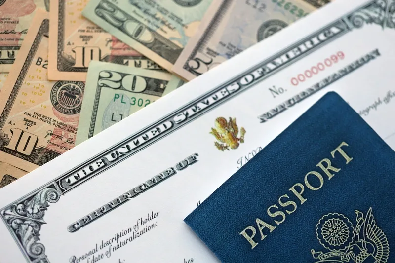 A U.S. Certificate of Naturalization and a blue U.S. passport on top of a pile of American currency.
